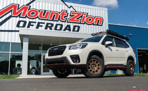 White 2019 Subaru Forester Sport with method wheels and falken tires on 2019 subaru forester sport with roof basket in front of the mount zion shop sign