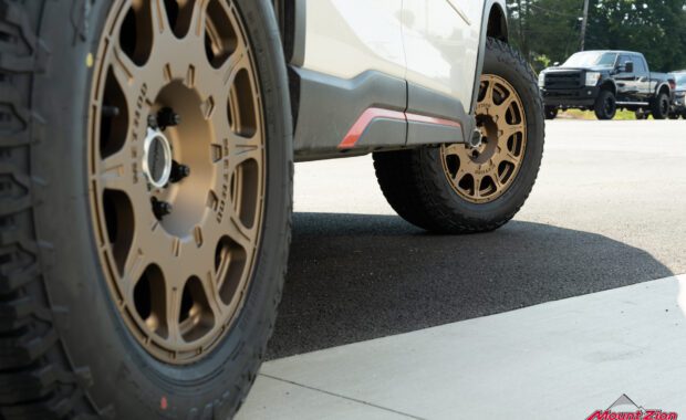 gold method wheels on white subaru with black f250 in background