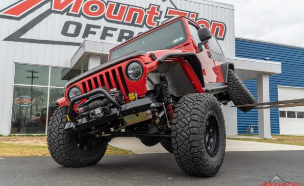 2005 two door jeep wrangler unlimited rubicon with Nitto tires and american racing wheels warn winch and metal cloak fender flares and side steps being lifted by fork lift in rear driver side tire