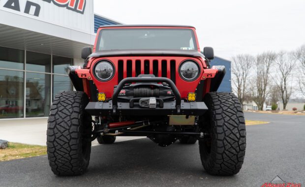 2005 Red Jeep Rubicon with offroad bumper warn winch, baja designs amber fog lights front grille view
