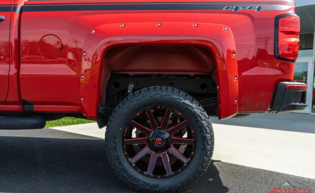 Rough Country lifted Red 2017 Chevy Silverado with red fender flares and black body stripe on Black and Red Fuel wheels rear driver side wheel well