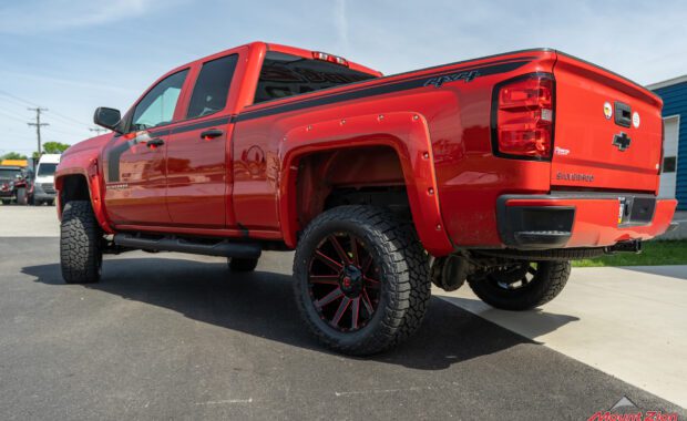 Rough Country lifted Red 2017 Chevy Silverado with red fender flares and black body stripe on Black and Red Fuel wheels rear driver tailgate view