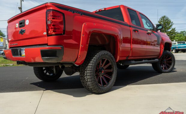Rough Country lifted Red 2017 Chevy Silverado with red fender flares and black body stripe on Black and Red Fuel wheels rear passenger tailgate view