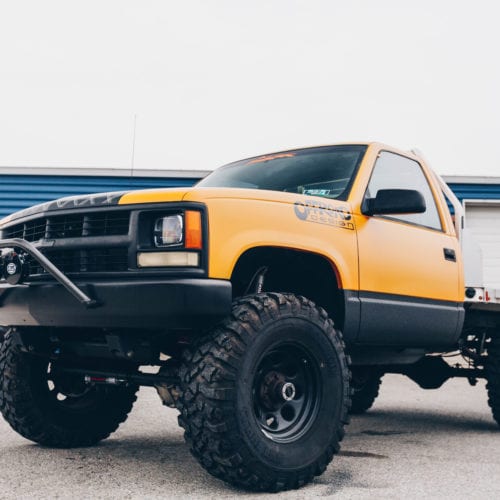 Offroad design yellow cab and flatbed truck with black wheels front driver side grille view