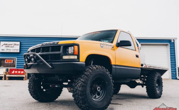 Offroad design yellow cab and flatbed truck with black wheels front driver side grille view