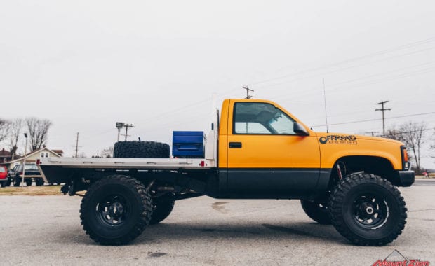 Offroad design yellow cab and flatbed truck with black wheels and blue tool box passenger side view