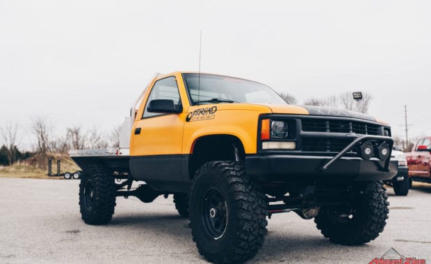 Offroad design yellow cab and flatbed truck with black wheels front passenger side grille view