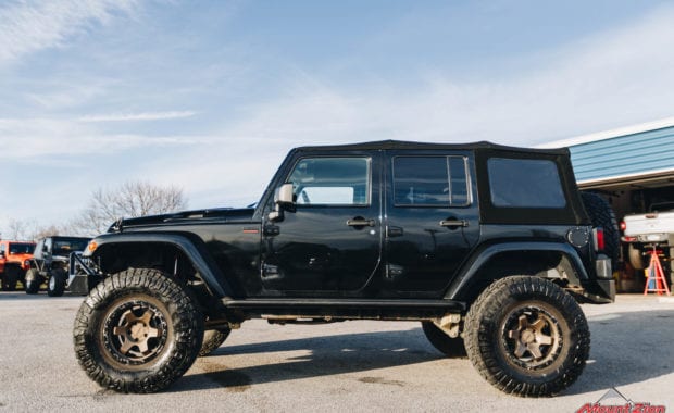 Black 4 dour soft top jeep with offroad style front bumper rotiform wheels and Nitto tires driver side view