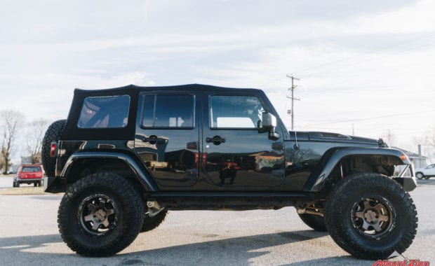 Black 4 dour soft top jeep with offroad style front bumper rotiform wheels and Nitto tires passenger side view