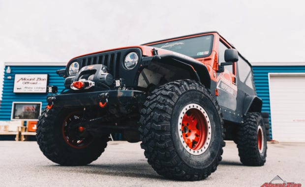 Rino linings branded two door jeep with red wheels and warn winch low front driver side grille view