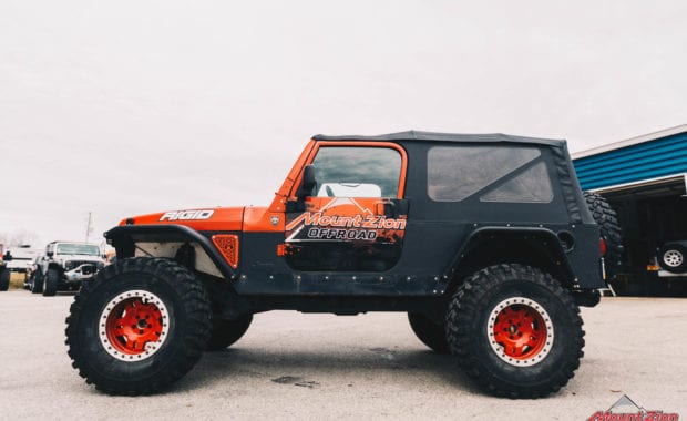 Rino linings branded two door jeep with red wheels and warn winch driver side view