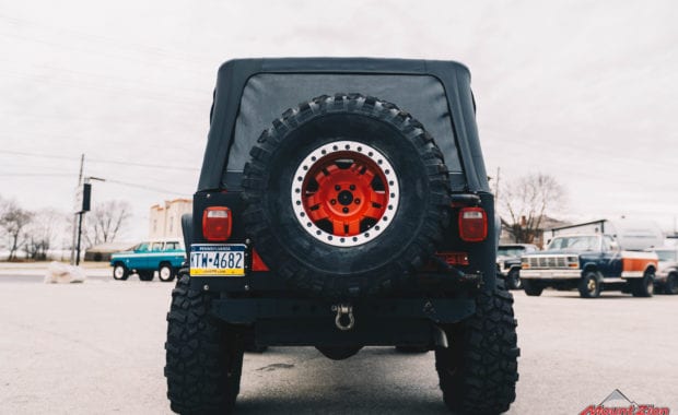 Rino linings branded two door jeep with red wheels and warn winch rear tailgate view
