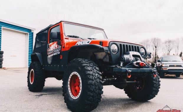 Rino linings branded two door jeep with red wheels and warn winch front passenger side grille view