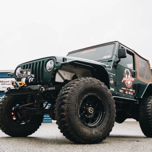 Green two door soft top jeep with Mount Zion offroad branding and winch front driver side grille view