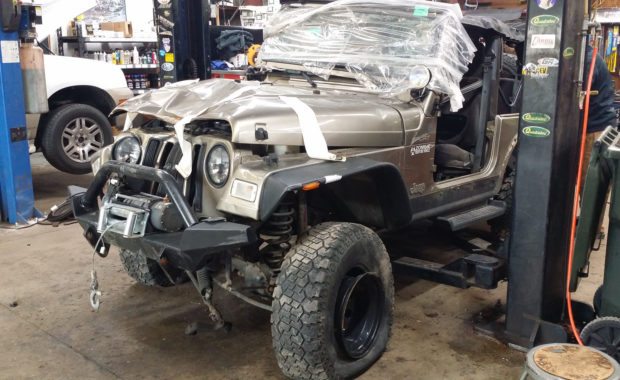 mangled jeep in shop bay with plastic on windshield tape on hood, flat tire