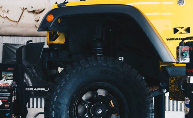 Yellow Wrangler on lift with fuel wheels driver side front end