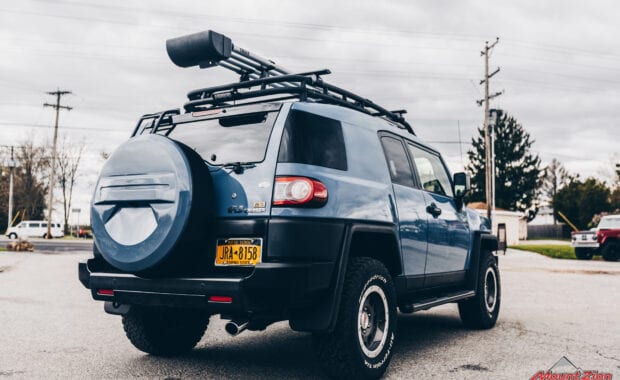 Blue FJ cruiser with roof rack rear passenger side tailgate view
