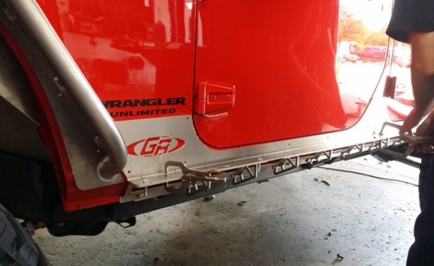 Tech installing sliders on Red Jeep
