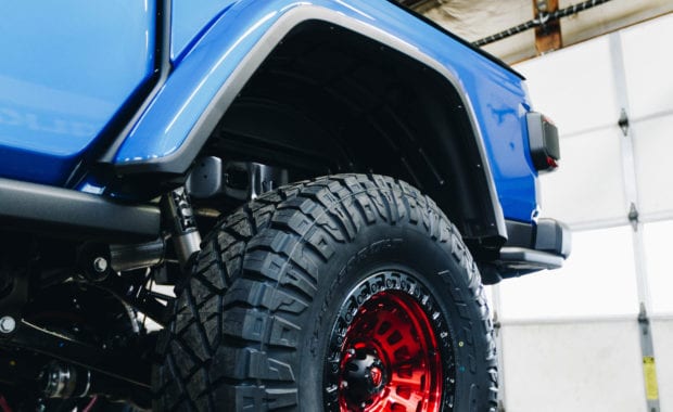 Blue Jeep Gladiator soft top with Red fuel wheels off ground in garage